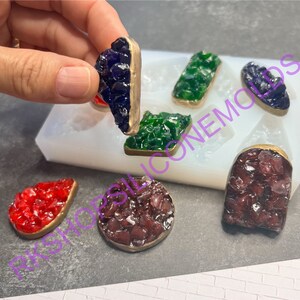 May include: Six resin crystal shapes in various colors, including red, green, purple, and brown, are displayed on a white silicone mold. Each crystal shape has a gold-colored metal rim.