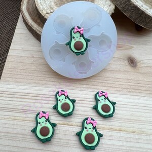 May include: A silicone mold with five cavities shaped like avocados with pink bows. There are four finished avocado-shaped charms with pink bows.