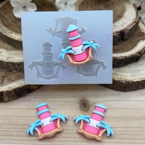 May include: Two pink and blue lighthouse charms with palm trees, made from silicone molds. The molds are shown in the background.