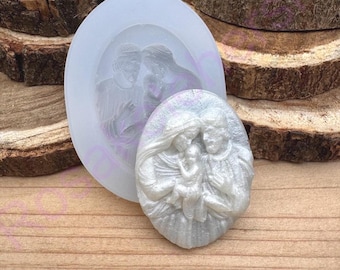 Könnte beinhalten: Eine transparente Silikonform und ein fertiger Resin-Guss einer religiösen Szene. Die ovale Form hat ein detailliertes Relief einer Familie. Der Resin-Guss ist perlmuttweiß und zeigt eine Familie, die ein Baby hält.