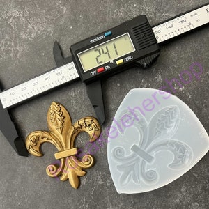 May include: A gold-colored metal fleur-de-lis design measuring 2.41 inches. A silicone mold of the design is shown next to it.