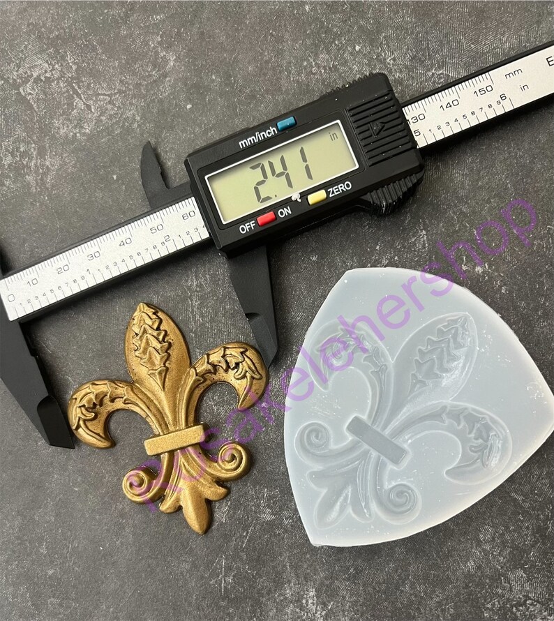 May include: A gold-colored metal fleur-de-lis design measuring 2.41 inches. A silicone mold of the design is shown next to it.