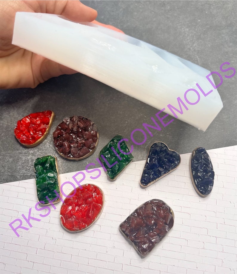 May include: A clear silicone mold for making resin jewelry. The mold is shown with several finished pieces of jewelry, including a red, green, and blue heart-shaped piece, a round piece, and a rectangular piece.