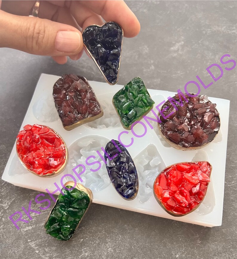 May include: Silicone mold with eight different shapes for making resin jewelry. The mold is white and has a variety of shapes, including a heart, a rectangle, an oval, and a teardrop. The mold is filled with colorful resin pieces.