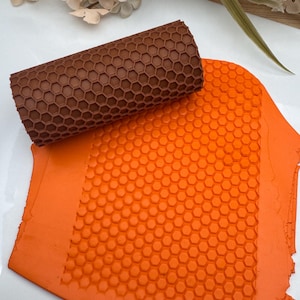 May include: A brown rolling pin with a honeycomb pattern is used to create a honeycomb pattern on a sheet of orange fondant.