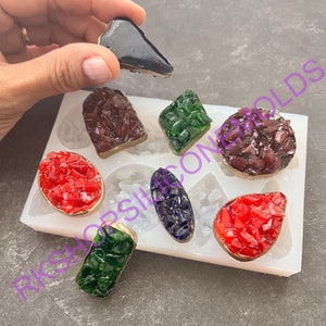 May include: A white silicone mold with eight different shapes for making resin jewelry. The mold contains a variety of shapes, including a teardrop, a rectangle, a square, and a circle. The mold is filled with colorful resin pieces.