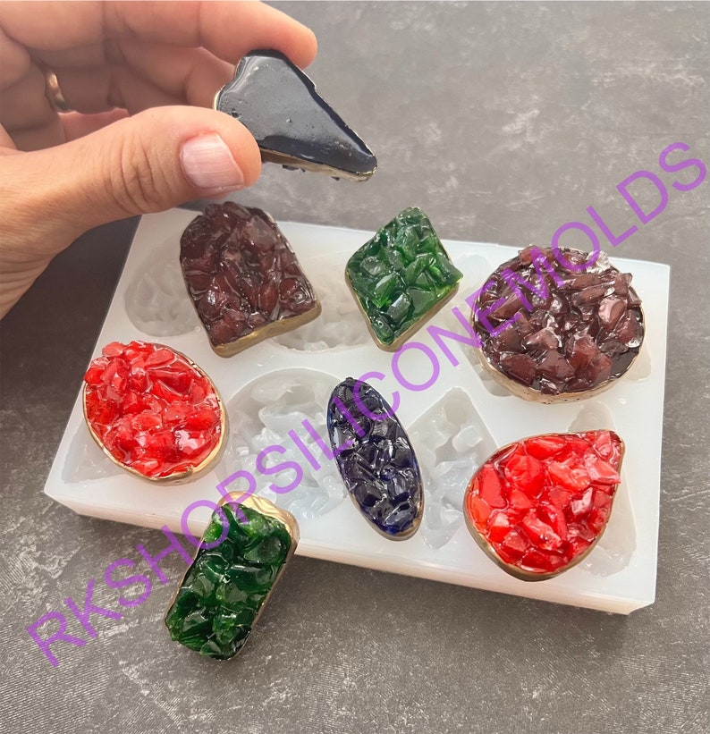 May include: A white silicone mold with eight different shapes for making resin jewelry. The mold contains a variety of shapes, including a teardrop, a rectangle, a square, and a circle. The mold is filled with colorful resin pieces.