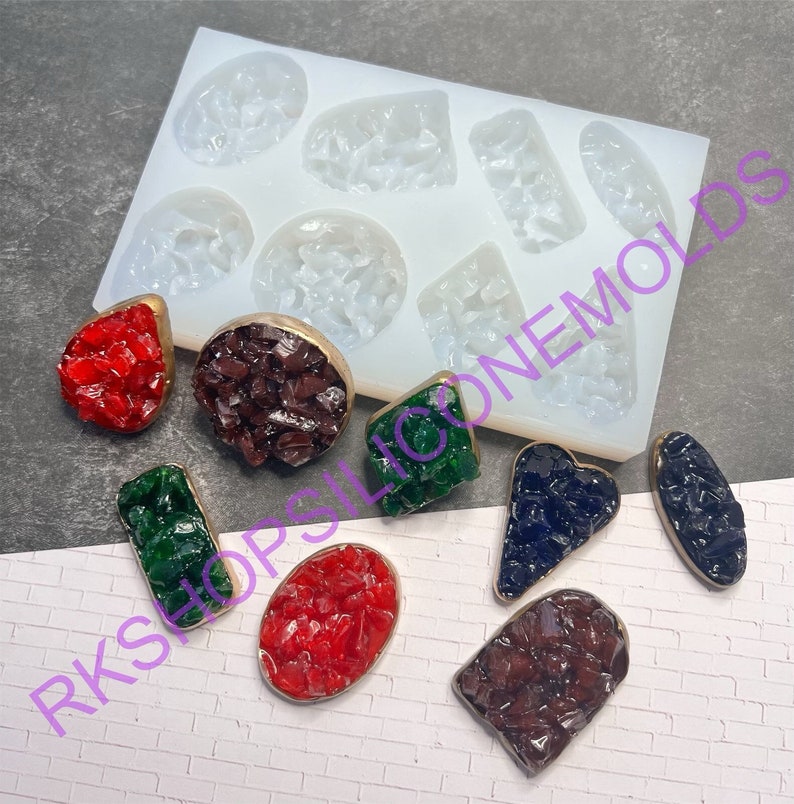 May include: A silicone mold with 10 different shapes for making resin jewelry. The mold is white and the shapes are clear. There are 10 finished resin pieces in various colors and shapes, including red, green, blue, and brown.
