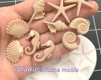 May include: A white silicone mold with various sea life shapes, including starfish, seashells, and seahorses. The mold is on a table with a hand holding the finished resin pieces.