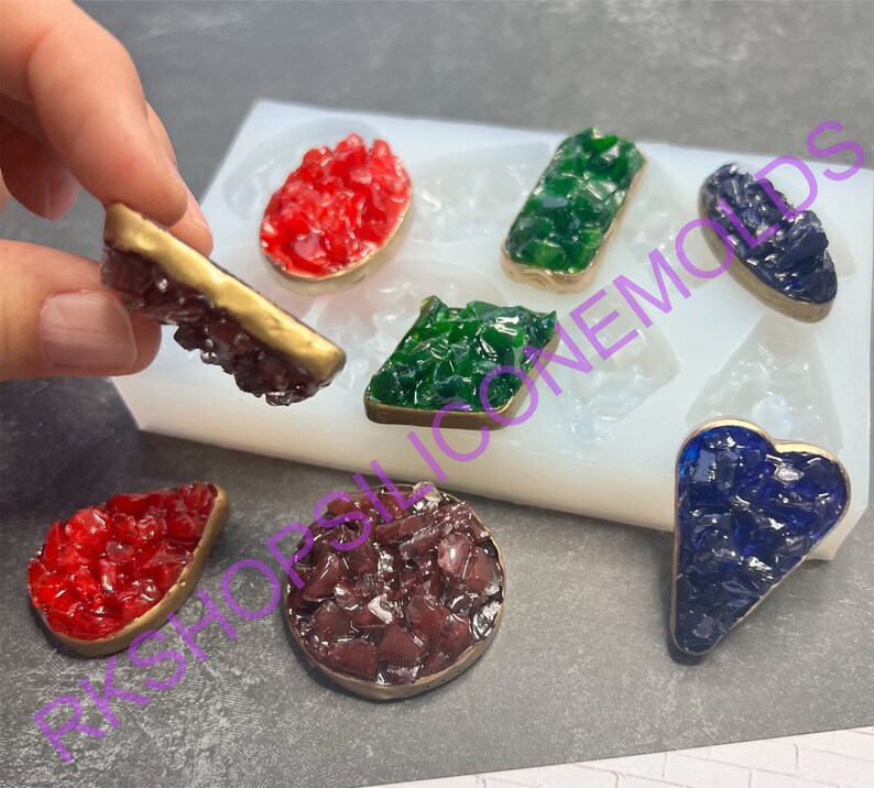 May include: Silicone mold with six different shapes for making resin jewelry. The mold is filled with red, green, blue, and brown resin pieces. The resin pieces are shaped like a heart, a rectangle, a diamond, a circle, and two teardrop shapes.