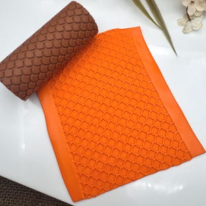 May include: A brown silicone rolling pin with a textured pattern and an orange silicone mat with a repeating pattern of small, rounded shapes.