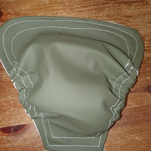 May include: A green waterproof diaper cover with white stitching. The cover has a gathered elastic waistband and a snap closure.