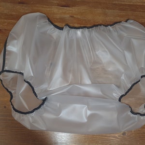 Puede incluir: Una cubierta de pañal de plástico transparente con ribete elástico negro alrededor de los bordes.