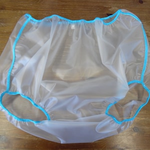 Puede incluir: Un pañal de plástico transparente con ribete azul. El pañal está hecho de un material delgado y flexible y tiene una cintura elástica fruncida.