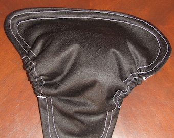 May include: Black fabric item with white stitching along the edges. The item has a gathered section and a curved shape. The stitching is a bright white against the dark fabric. The item appears to be a protective cover or liner.