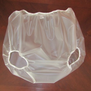Puede incluir: Un pañal de plástico transparente con elástico blanco alrededor de las aberturas de las piernas.
