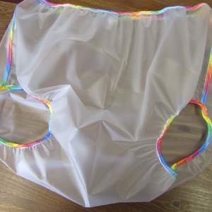 Puede incluir: Pañal reutilizable de plástico transparente con ribete de arcoíris. El pañal está hecho de un material impermeable y tiene una cintura elástica fruncida.