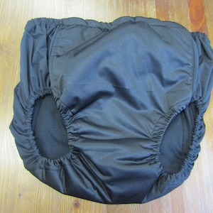 May include: Black, elastic-waisted protective underwear. The garment has openings for the legs and is made of a smooth, shiny fabric. The underwear is designed to be worn over other garments.