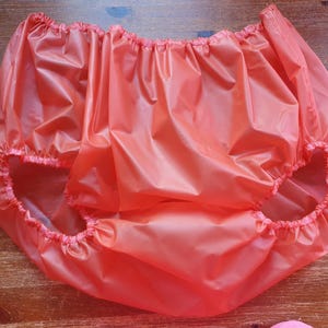 Puede incluir: Una cubierta de pañal de plástico de color naranja brillante con elástico alrededor de las piernas y la cintura.