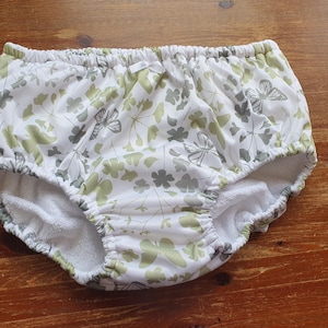 Puede incluir: Pañal de tela blanco con un estampado floral y de mariposas en verde y gris. El pañal tiene cintura y aberturas para las piernas elásticas. El interior es blanco y absorbente. Diseñado para bebés y niños pequeños.
