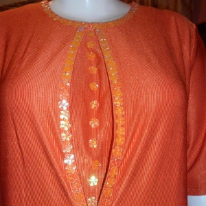 Könnte beinhalten: Ein leuchtend oranges Kleid mit V-Ausschnitt und einem dekorativen Besatz aus orangefarbenen und goldenen Pailletten.