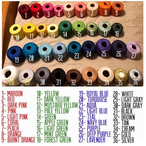 May include: A color chart of 36 different colors of embroidery floss. The floss is wound around small spools and labeled with numbers 1 through 36. Each color is also labeled with a name, such as maroon, red, dark pink, pink, light pink, coral, peach, orange, burnt orange, yellow, dark yellow, mustard yellow, pale yellow, green, apple green, light green, mint green, forest green, royal blue, turquoise, aqua, light blue, teal, navy blue, purple, deep purple, lavender, white, light gray, dark gray, black, brown, tan, cream, gold, and silver.
