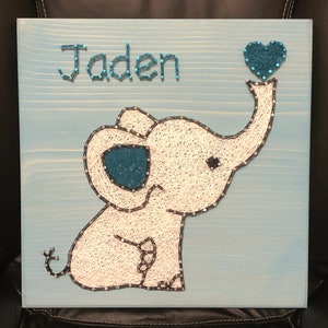 May include: A blue wooden sign with a white string art elephant holding a blue heart that says "Jaden" above the elephant.