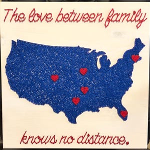 May include: A square wooden sign featuring a string art map of the United States in blue thread with five red heart accents. The text "The love between family" is at the top and "knows no distance." is at the bottom in red string lettering.