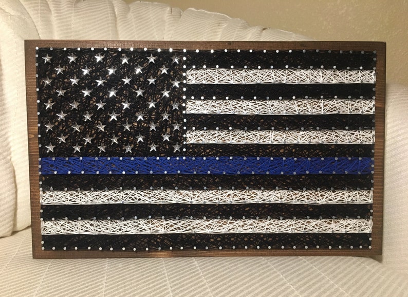 May include: A wooden framed string art piece depicting the American flag with a blue line running horizontally across the middle of the flag.