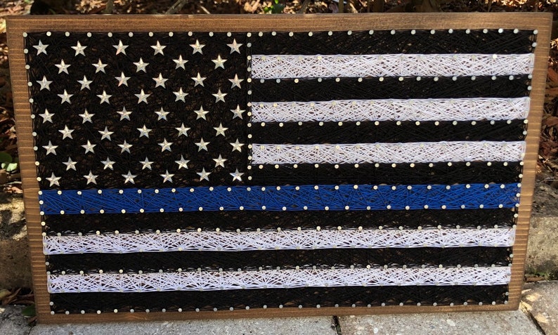 May include: A wooden framed string art piece depicting the American flag with a blue line, representing support for law enforcement.