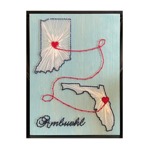 May include: A blue and white string art piece depicting the states of Indiana and Florida connected by a red string with hearts at the center of each state. The text "Ambush" is written in blue string art below the states.