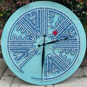 May include: A blue and white clock with a unique design. The clock face is made of string and has a red heart in the center. The clock hands are black.