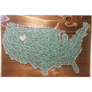 May include: A teal blue string art piece depicting the outline of the United States of America. A small white heart is in the center of the map, representing a location.