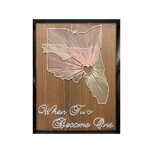 May include: String art of the state of Ohio with a heart in the center. The string art is on a wooden background and the words "When Two Become One" are written below the art.