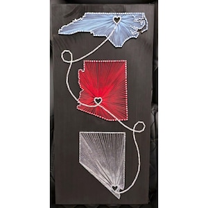 May include: A dark wooden board featuring three state shapes outlined in nails and filled with string art. The top shape is light blue, the middle is red, and the bottom is white. A single white string connects heart-shaped cutouts in each state.