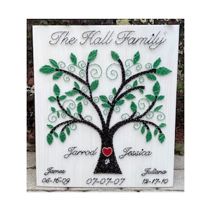 May include: A white wooden sign with a black string art tree design. The tree has green leaves and a red heart at the base. The text "The Hall Family" is at the top of the sign. Below the tree are the names "Jarrod", "Jessica", "James", "Juliana" and their corresponding dates.
