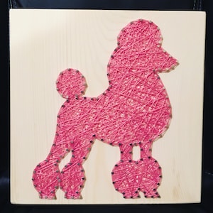 May include: Pink string art of a poodle on a wooden background.