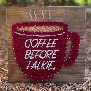 May include: A red coffee cup with steam coming from the top, with the words "Coffee Before Talkie" in white string art on a wooden background.