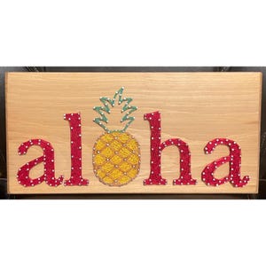 May include: String art of the word "Aloha" with a pineapple in the center. The letters are red and the pineapple is yellow with green leaves.