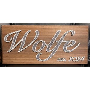 May include: A wooden sign with the name "Wolfe" in a cursive font, created with string art. The sign also includes the text "est. 2024".