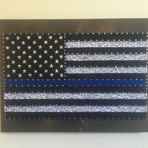 May include: A string art rendition of the American flag with a blue line, representing support for law enforcement.