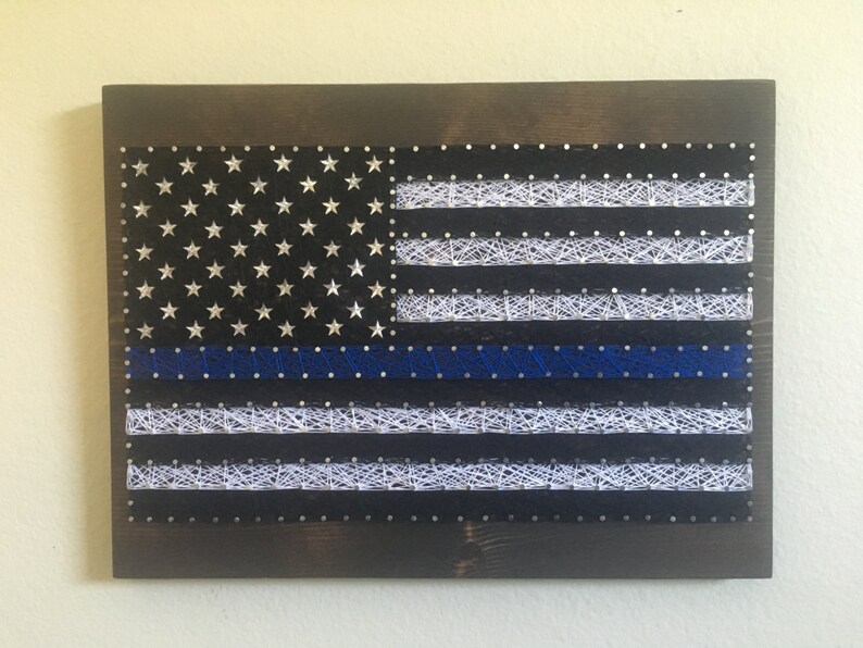 May include: A string art rendition of the American flag with a blue line, representing support for law enforcement.