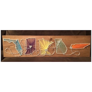 May include: String art wall hanging featuring the outlines of five states in the USA, each filled with colorful string. The states are Florida, Maryland, Minnesota, Georgia, and Tennessee. The string art is on a wooden background.