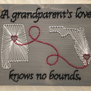 May include: A gray wooden sign with the text "A grandparent's love knows no bounds."  The sign features a string art design of the states of Alabama and Florida connected by a red heart.
