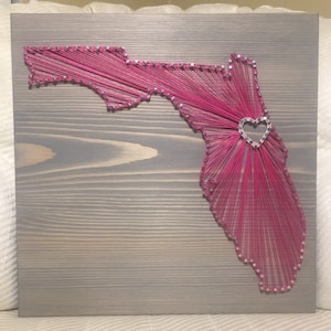 May include: Pink string art of the state of Florida with a silver heart in the center.