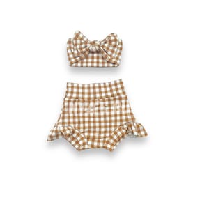 May include: A brown and white gingham baby outfit with a matching headband. The outfit includes a pair of shorts with a ruffled hem and a bow headband.