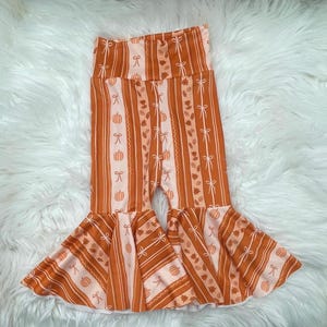 May include: Orange and white striped baby pants with a flared bottom. The pants feature a repeating pattern of pumpkins, bows, and leaves. The fabric has a soft, lightweight appearance, perfect for fall.