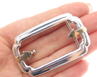 May include: A silver-tone rectangular buckle with a scalloped edge and gold-tone accents. The buckle has a decorative design and a classic shape, suitable for belts or other accessories.
