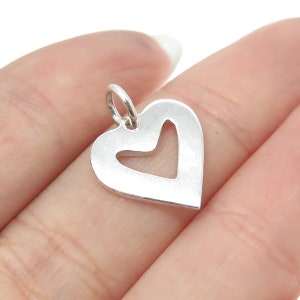 May include: A silver charm in the shape of a heart with a smaller heart cut out of the center.