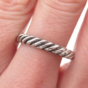 May include: A silver-colored ring with a twisted rope design. The ring is shown close-up, highlighting the texture and detail of the metal. The ring is a simple band style, suitable for everyday wear.